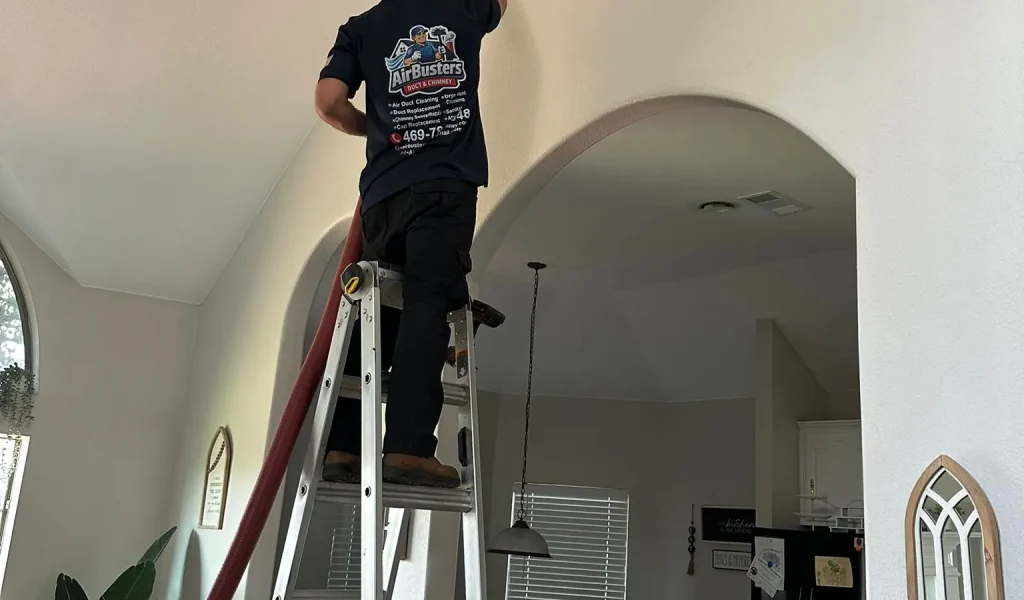 Air Busters technician cleaning a ceiling air vent in a DFW home