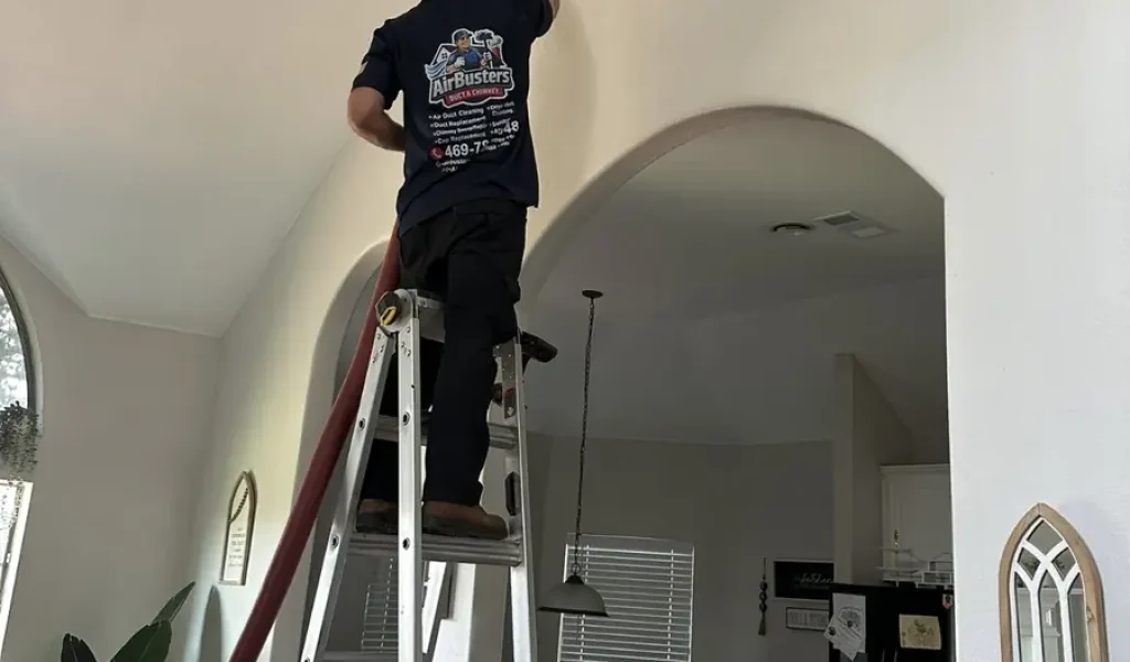 Air Busters technician on a ladder cleaning a ceiling air vent in DFW